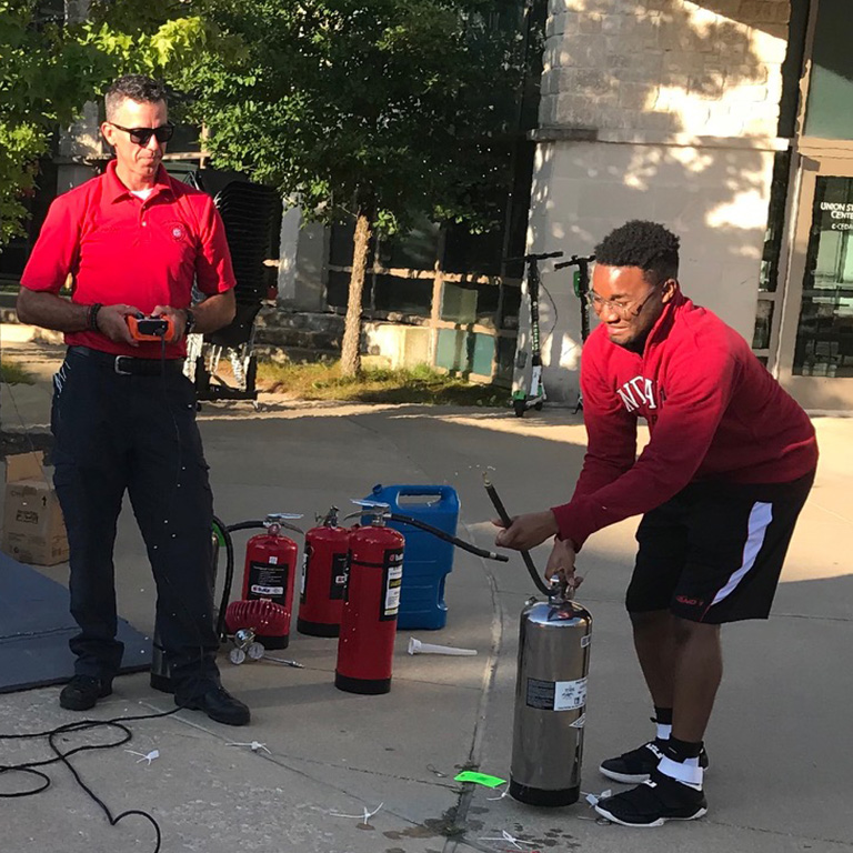 A firefighter instructs a student on how to use a fire extinguisher in front of the Union Student Center.