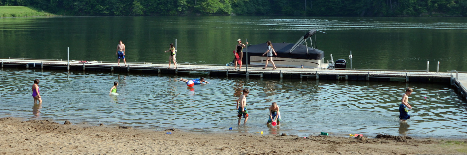 People standing on a dock, swimming, and playing on a beach.