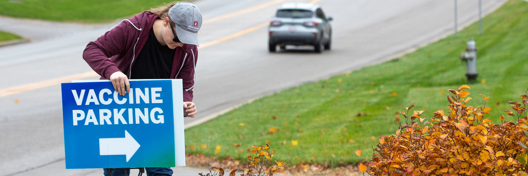 A woman in an embroidered IU EHS ball cap sets out signs for a vaccine clinic.