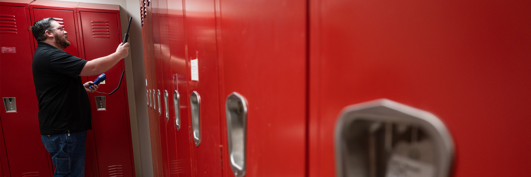 A row of IU lockers, forming a bright red, angular composition drawing the viewer's line of sight directly to the EHS worker inspecting them. 