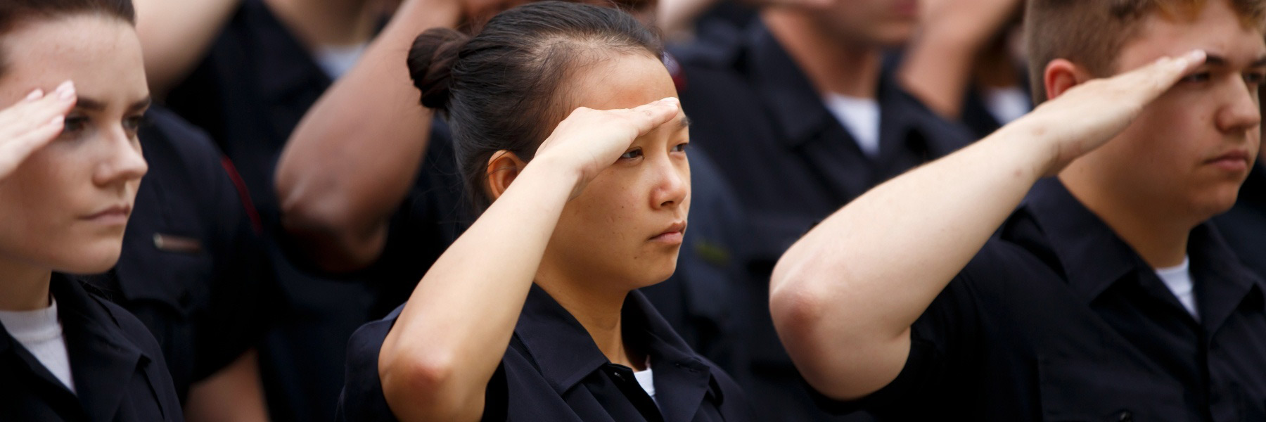 A woman in IUPD uniform salutes with other cadets at a ceremony. 