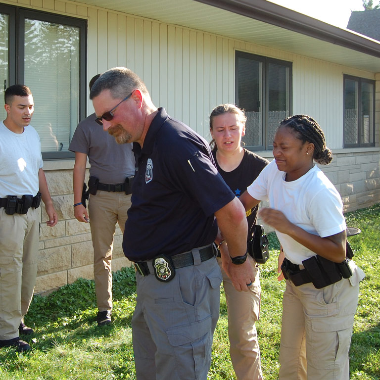 An IU Police Academy cadette practices restraint and cuffing on her instructor during a summer outdoor drill.