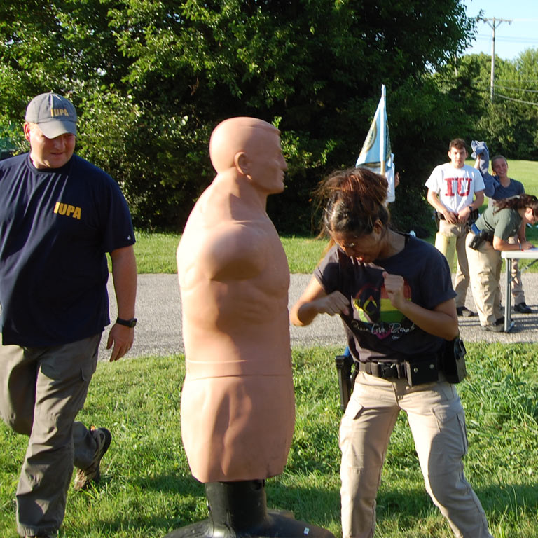 An IU Police Academy instructor inspects the form of a cadette practicing self-defense on a police dummy.