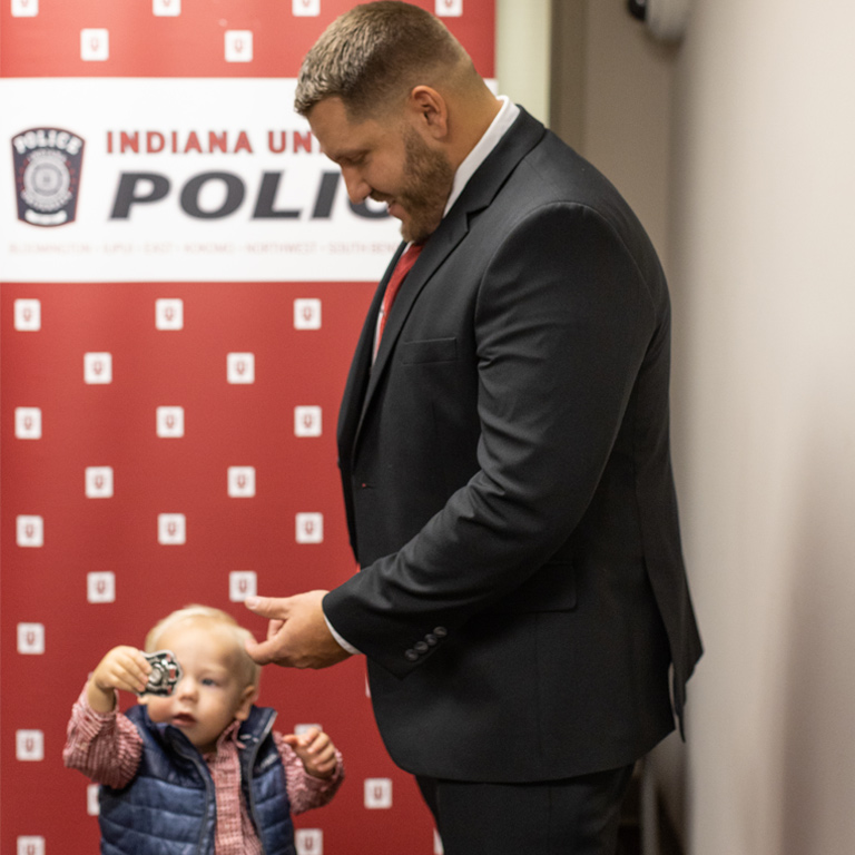 An adorable toddler wearing a checked pink shirt and a tiny blue puffer vest plays with his father's IUPD badge at a recent swearing-in ceremony. 