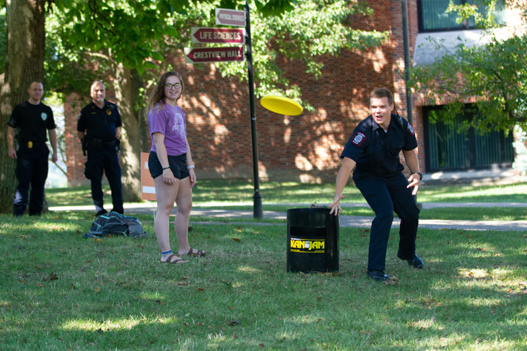 A young IUPD officer plays lawn frisbee in front of an audience of students and fellow officers, on the IU East campus.