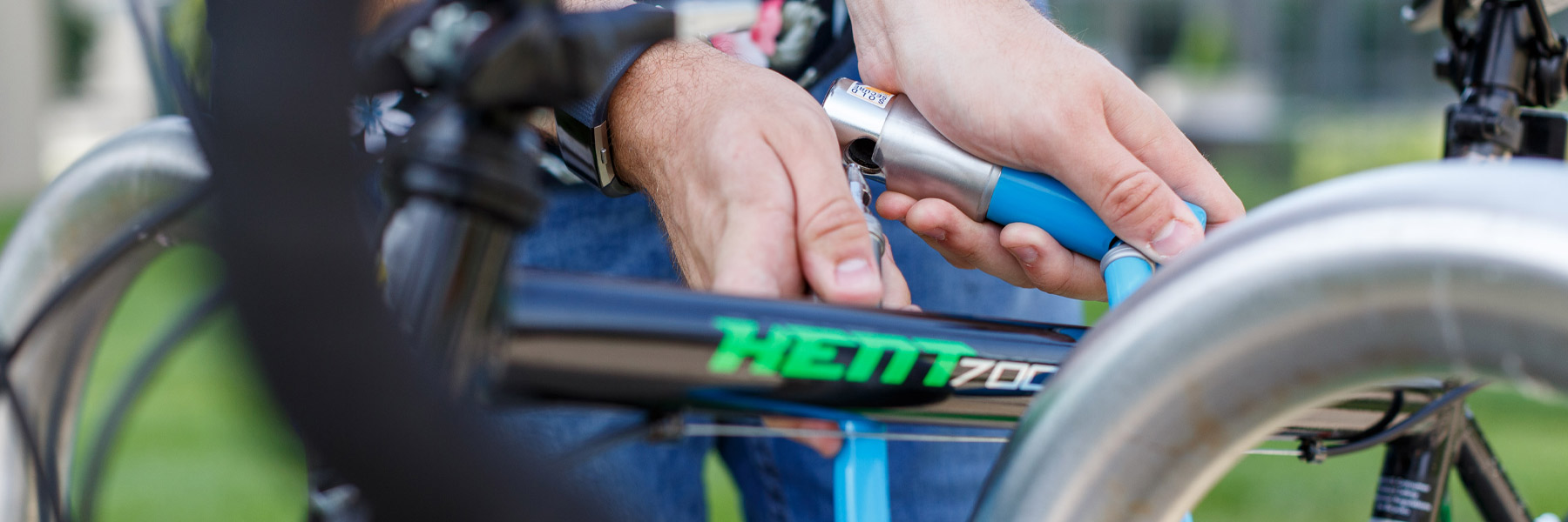 A brightly colored, shallow-focus close-up image of a young man securing his bicycle with a pastel blue U-lock.