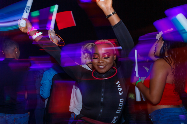 A young woman dressed for a night out dances while holding noisemakers and wearing glowsticks.