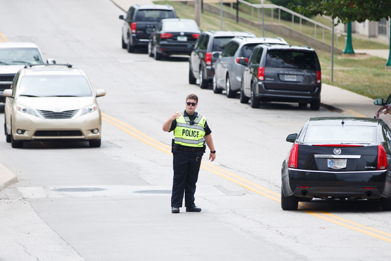 An IUPD officer in hi-visibility vest and uniform directs traffic on a warm summer's day.